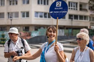 Frau hält Schild mit der Aufschrift '2 BOLERO nicko cruises' bei einer Stadttour mit mehreren älteren Personen