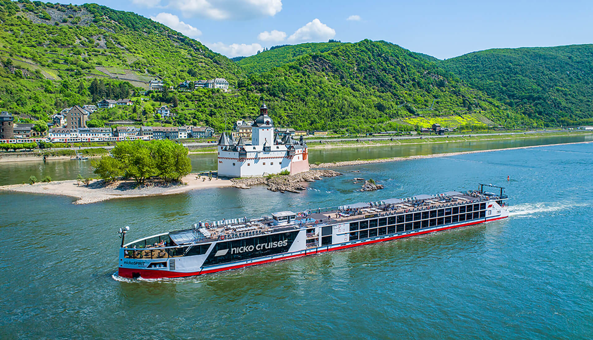 Flusskreuzfahrtschiff der Marke Nicko Cruises fährt auf dem Rhein vor der Burg Pfalzgrafenstein in einem bewaldeten Tal