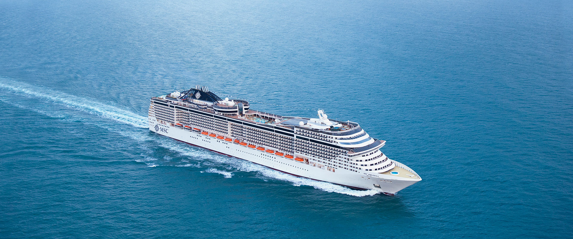 Kreuzfahrtschiff der Reederei MSC fährt auf offenem Meer unter blauem Himmel.