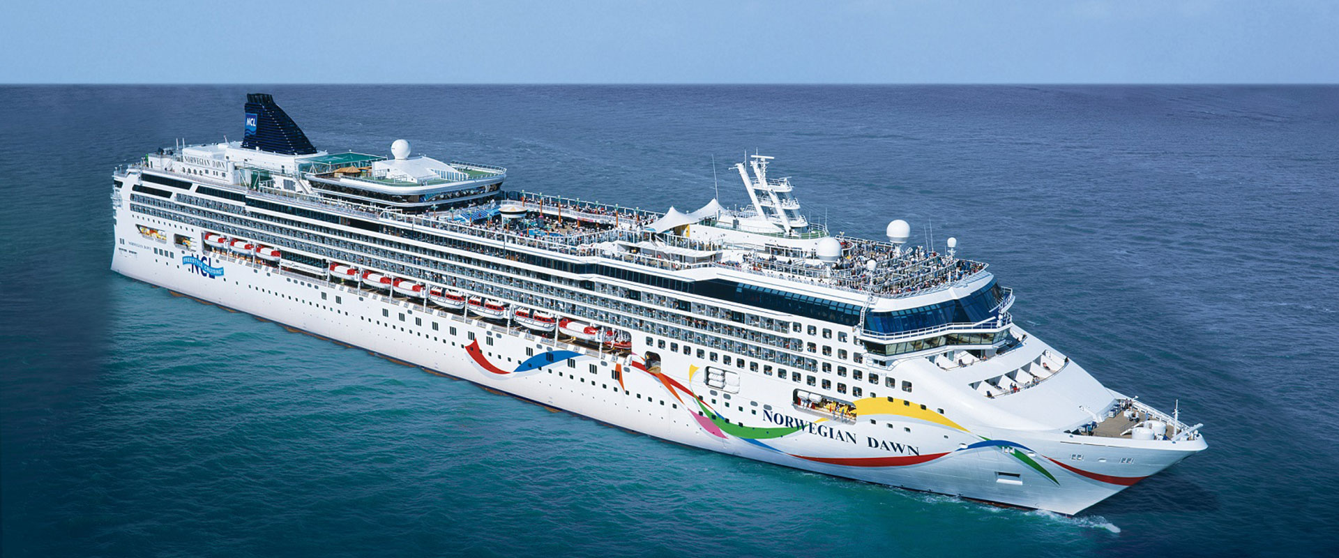 Die Norwegian Dawn von der Reederei Norwegian Cruise Line auf offener See bei klarem Himmel.