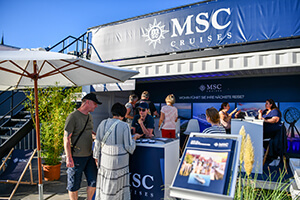 MSC Cruises Informationsstand mit mehreren Personen, Sonnenschirm und Werbebanner 'World's Best Mediterranean Resort'