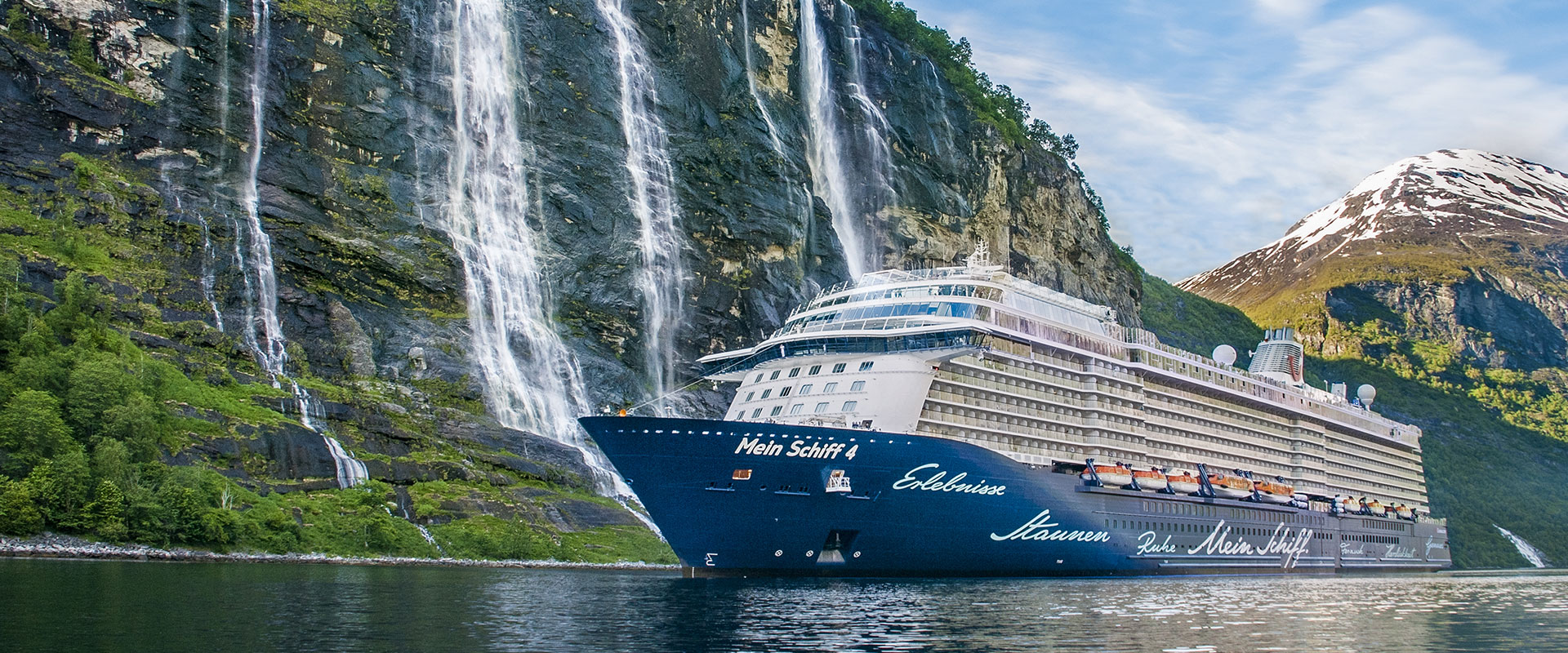 Kreuzfahrtschiff Mein Schiff 4 fährt in einem Fjord mit hohen Felswänden und mehreren Wasserfällen