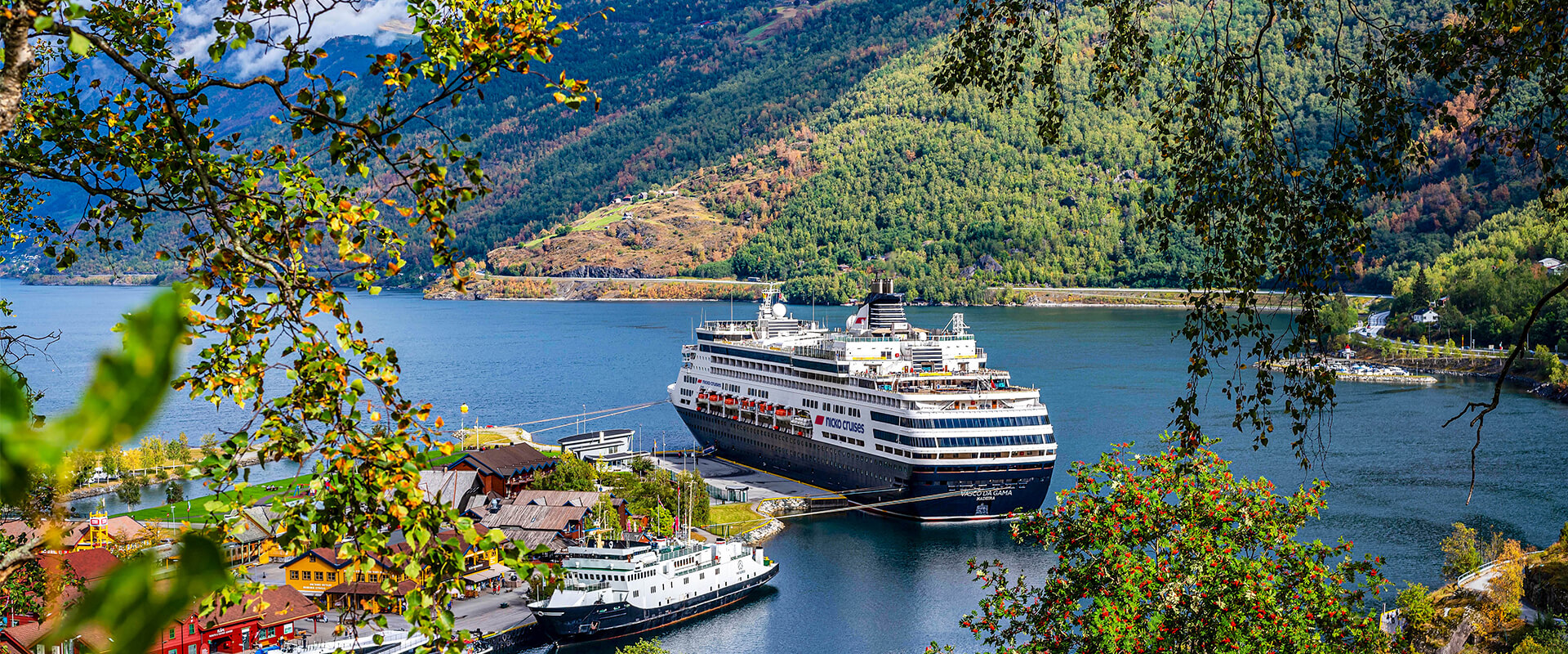 Kreuzfahrtschiff Vasco da Gama im Fjord, umgeben von grünen Bergen und kleinen Gebäuden am Ufer