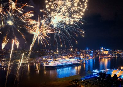 Feuerwerk über einem Hafen mit beleuchtetem Kreuzfahrtschiff und Stadt bei Nacht