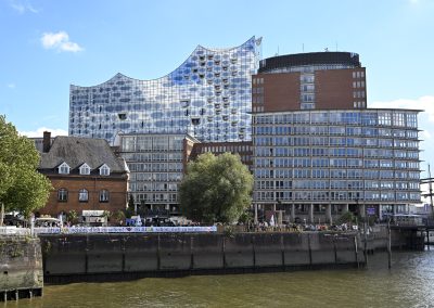 Menschenmenge auf einem Platz mit MSC-Fahnen, einem großen rot-weiß gestreiften Leuchtturmmodell und einer blauen Maskottchenfigur mit lachendem Gesicht.