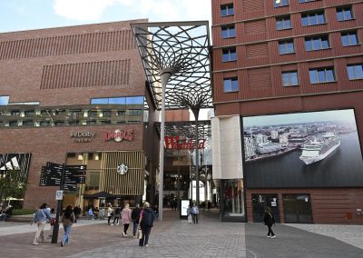 Eingang zum Einkaufszentrum mit überdachtem Bereich, Kinopolis- und Dolby-Cinema-Logos, mehreren Passanten und großem Bildschirm mit Kreuzfahrtschiff.